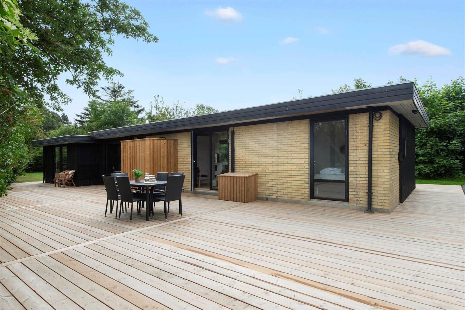 Modern villa with large wooden deck, terrace, and garden table. Surrounded by trees.