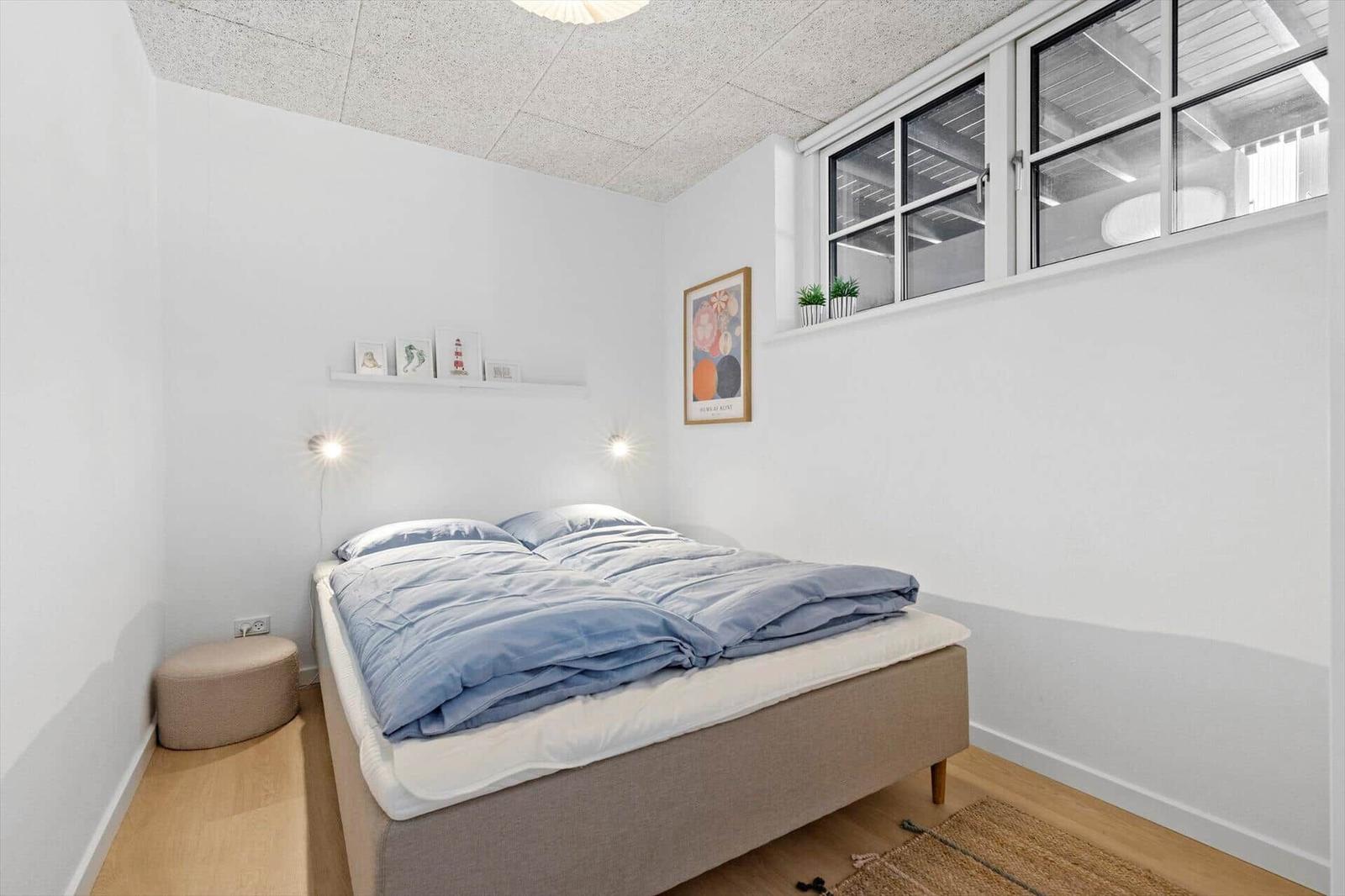 Bedroom with bed, wall shelf, and window. Wooden floor and white walls.