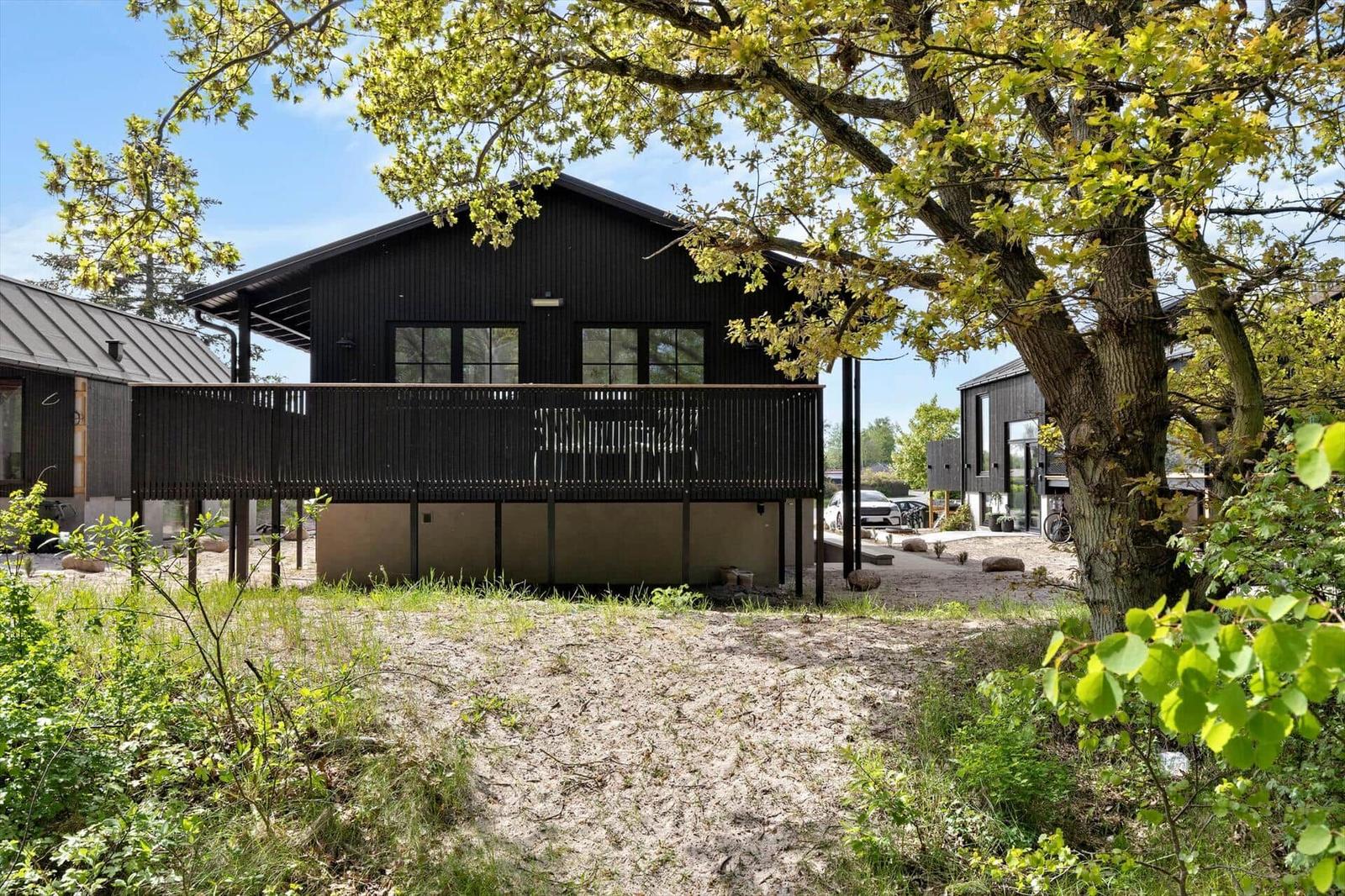 Black house with balcony, surrounded by trees and green areas.