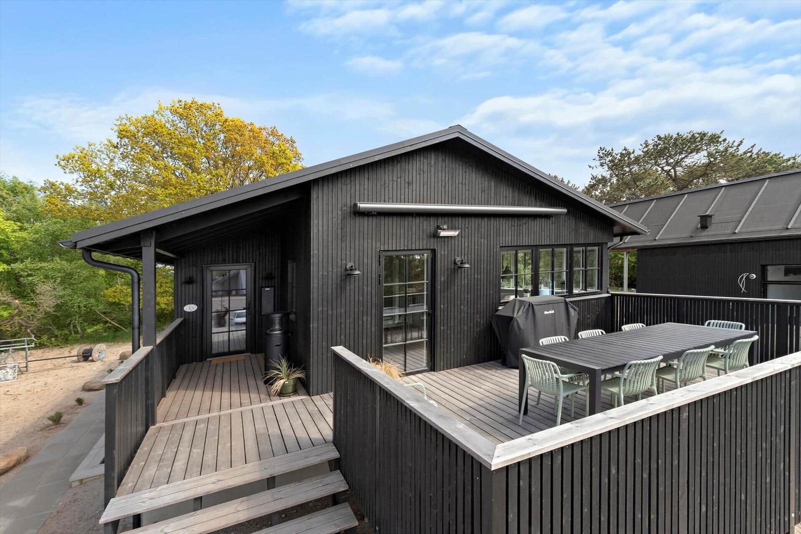 Black wooden house with terrace and outdoor seating area.