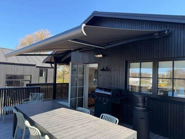 Deck with table, chairs, and grill under a sun shade.