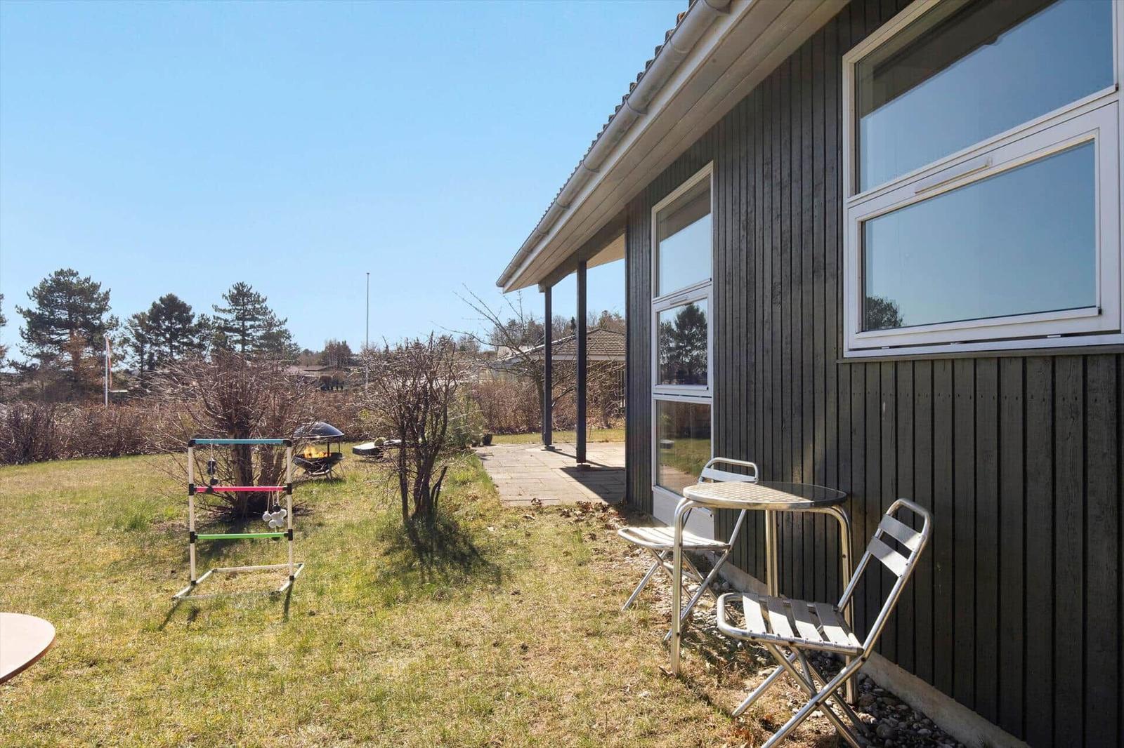 Haus mit Terrasse, Garten und Grillplatz. Kleiner Tisch mit zwei Stühlen.