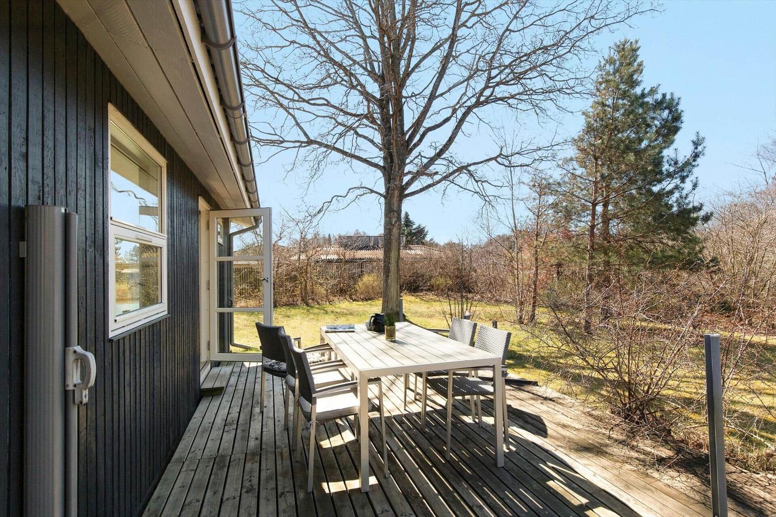 Terrasse mit Tisch und Stühlen neben einem Haus mit dunklem Holzverkleidung.