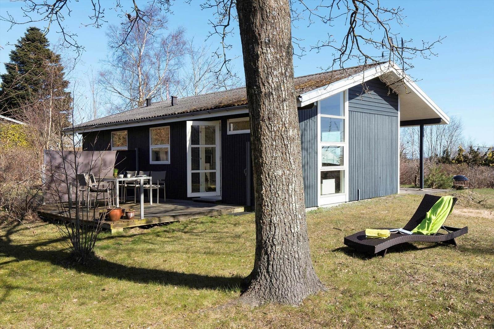 Ein Haus mit Terrasse und Liegestuhl im Garten. Bäume und Gras umgeben das Gebäude.