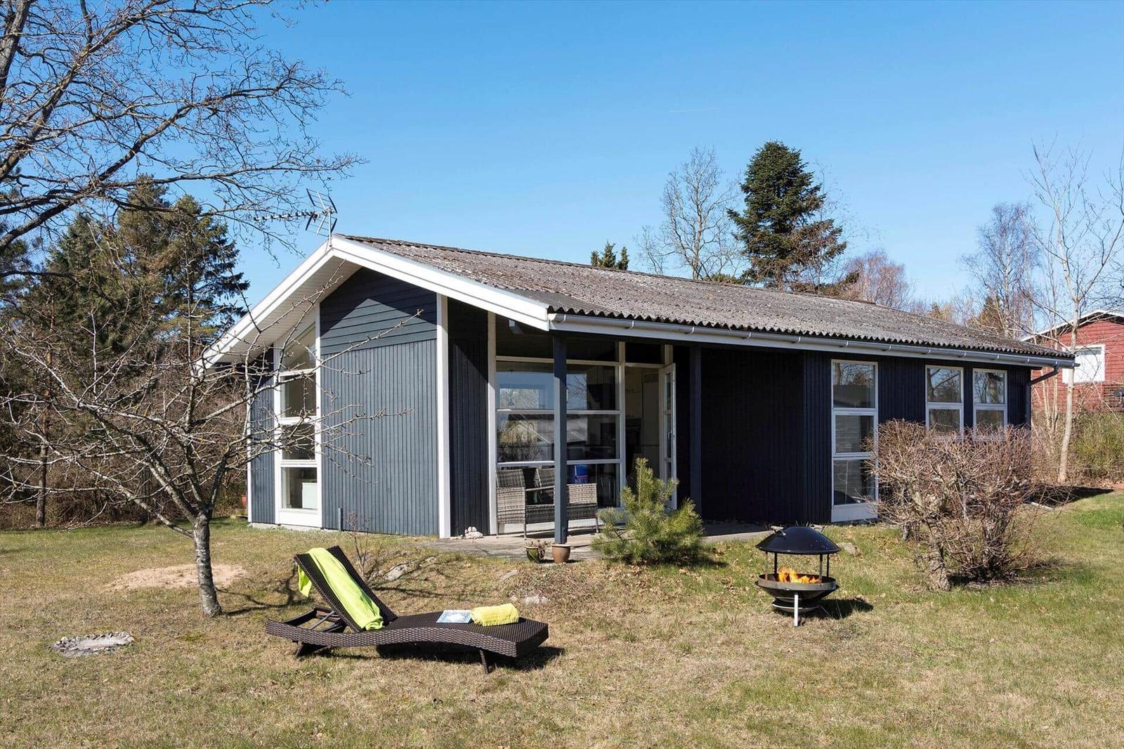 Ein Haus mit dunkler Fassade, großem Fensterbereich und Gartenbereich mit Liege und Grill.