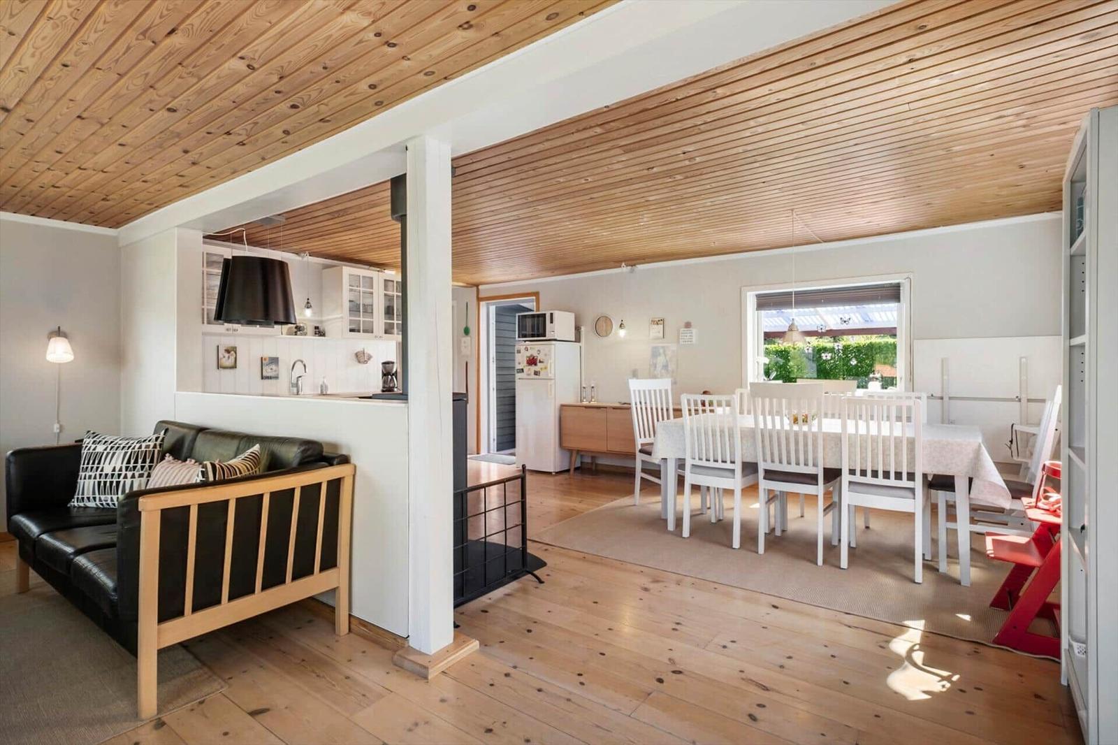 Living and dining area with wooden ceiling, sofa, dining table, and kitchen area.