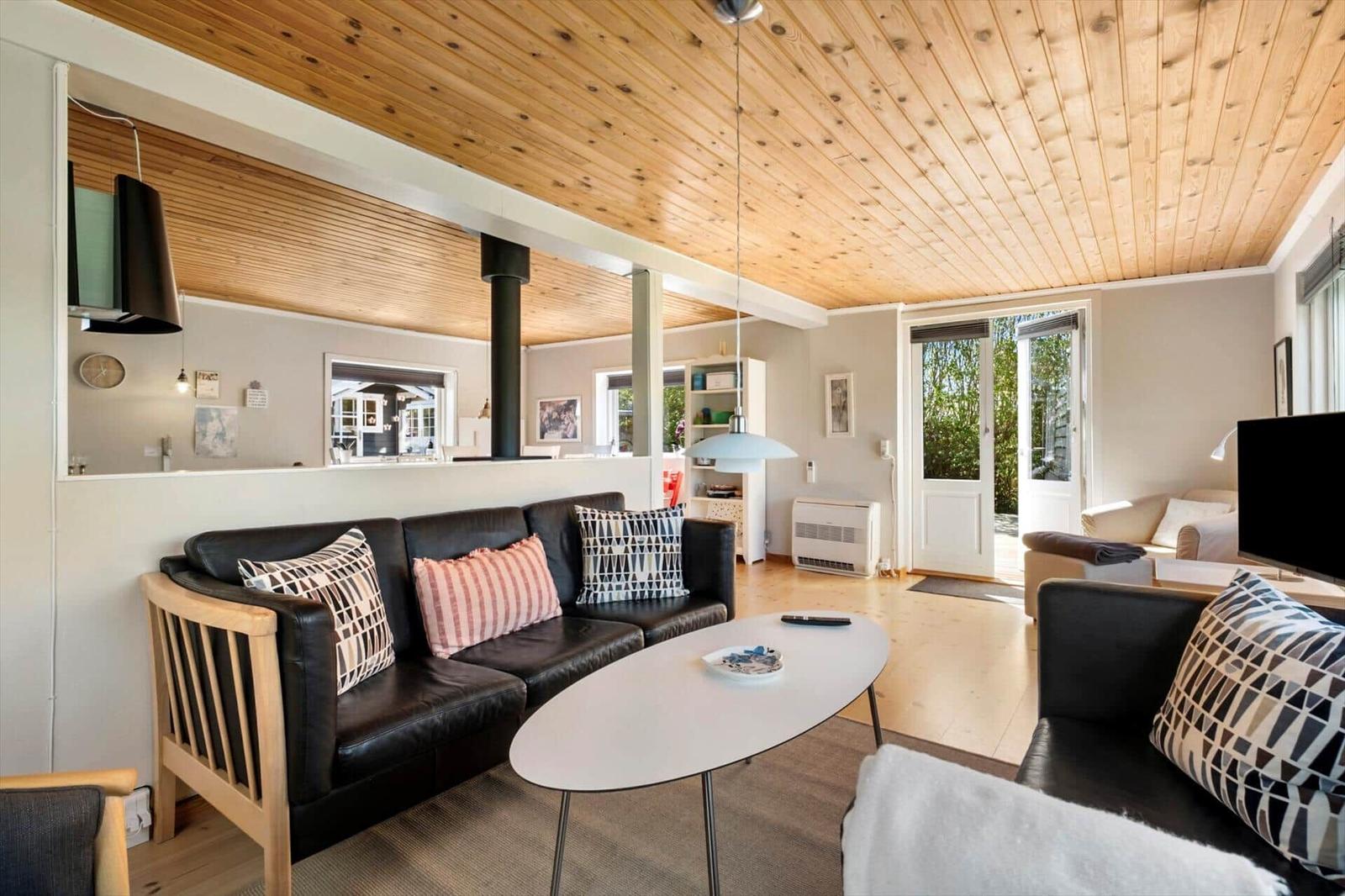 Living room with black sofas, wooden ceiling, and view to the terrace.
