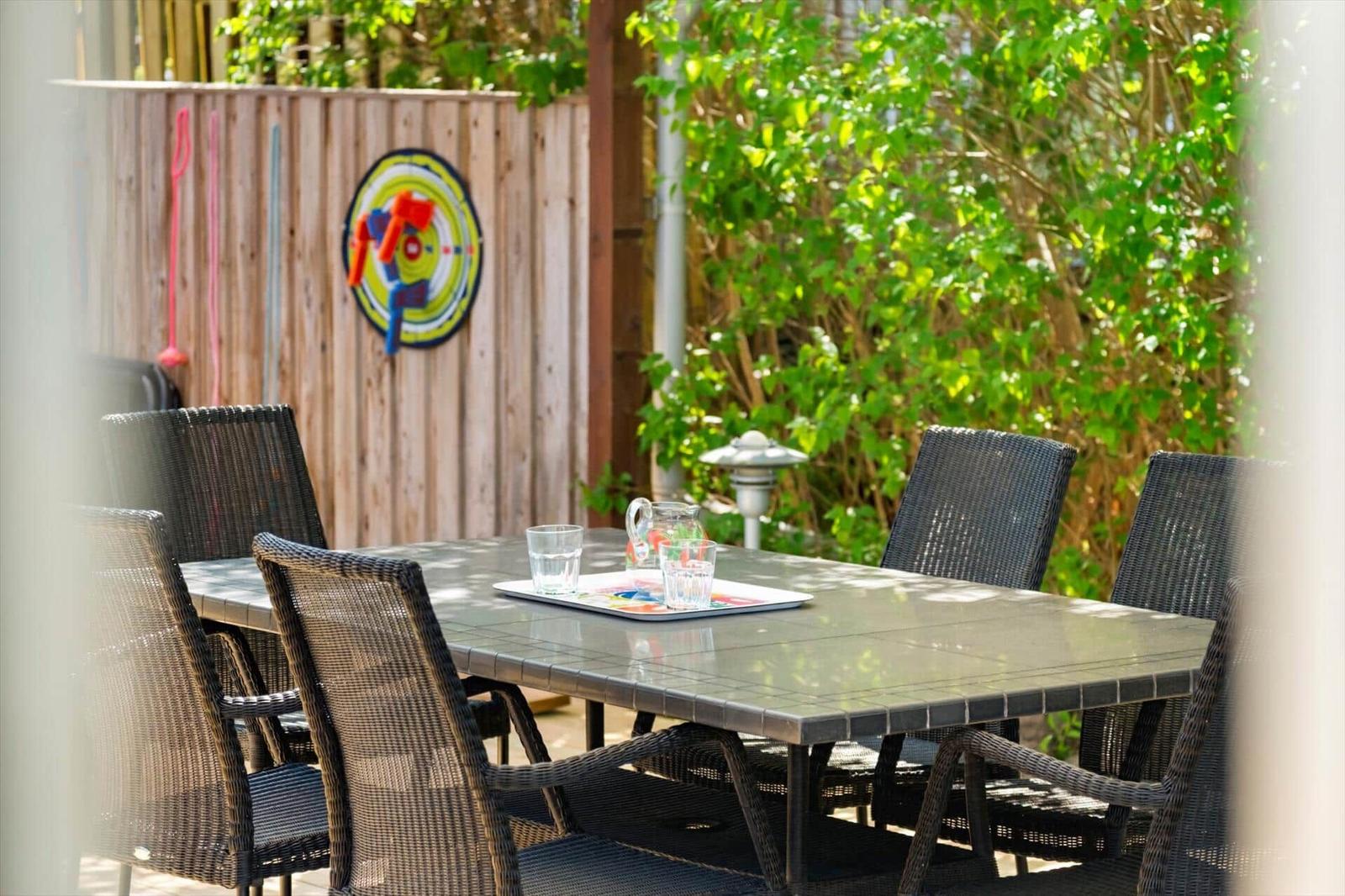Outdoor area with table and chairs, background with wooden fence and plants.