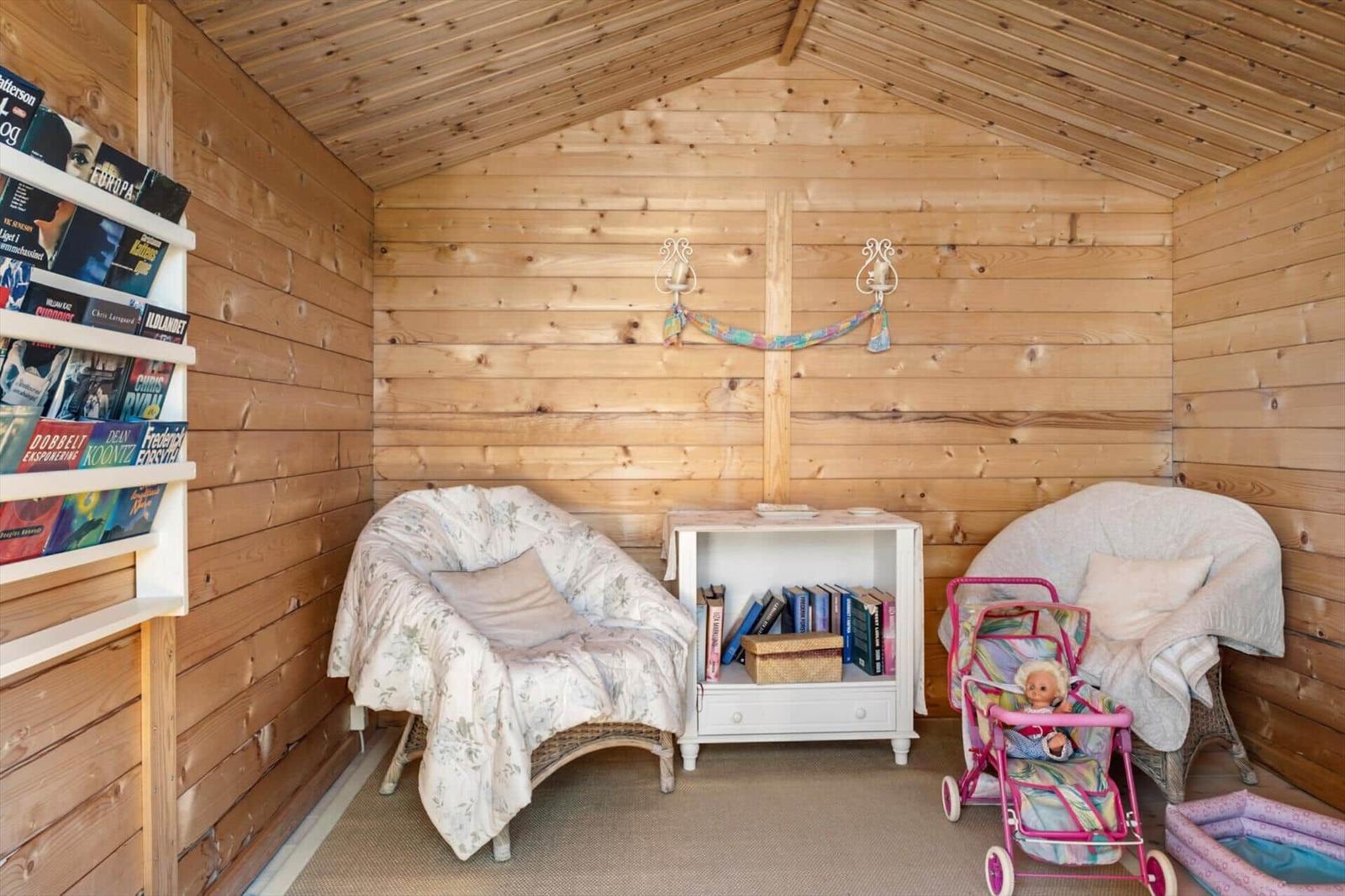 Wood-paneled room with two chairs, bookshelf, and baby stroller.