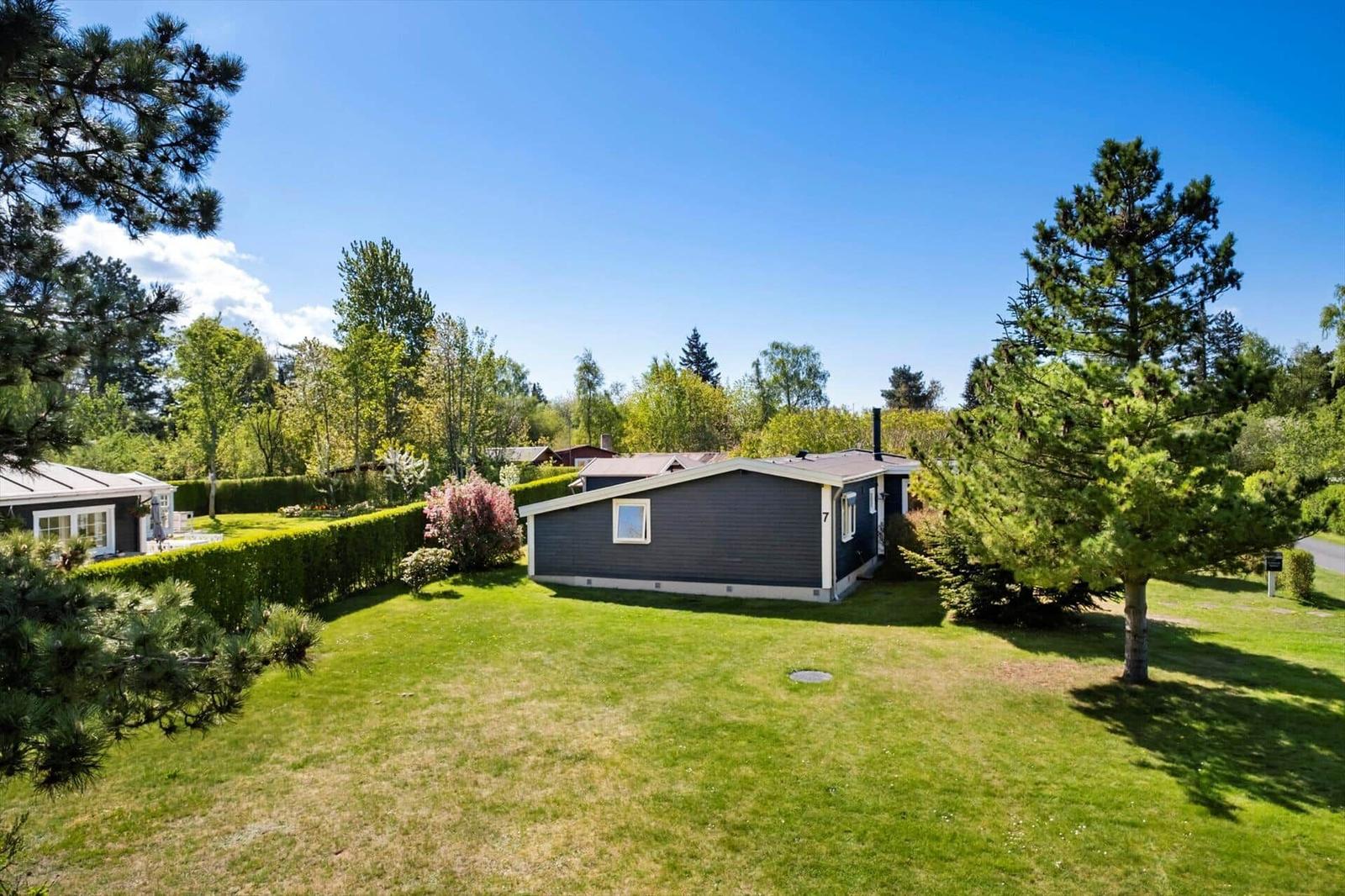 A dark blue holiday home with green lawn and trees in the background.