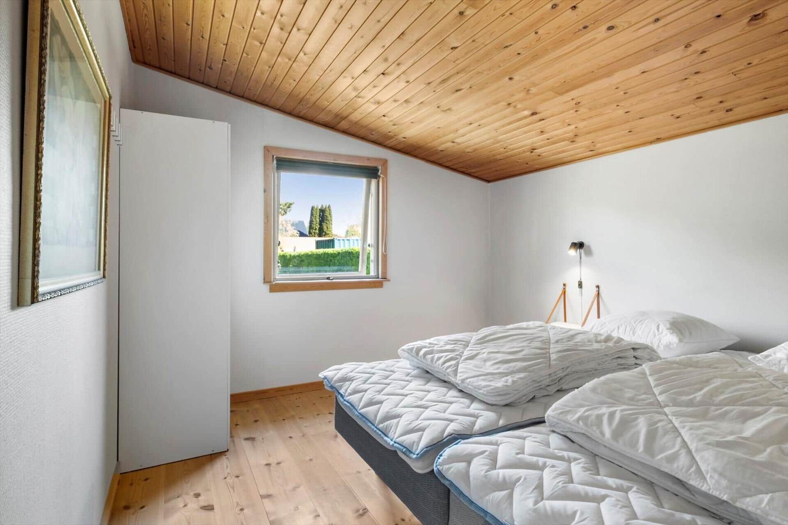 Bedroom with double bed, wooden ceiling, and window. Wall lamp and wardrobe are present.
