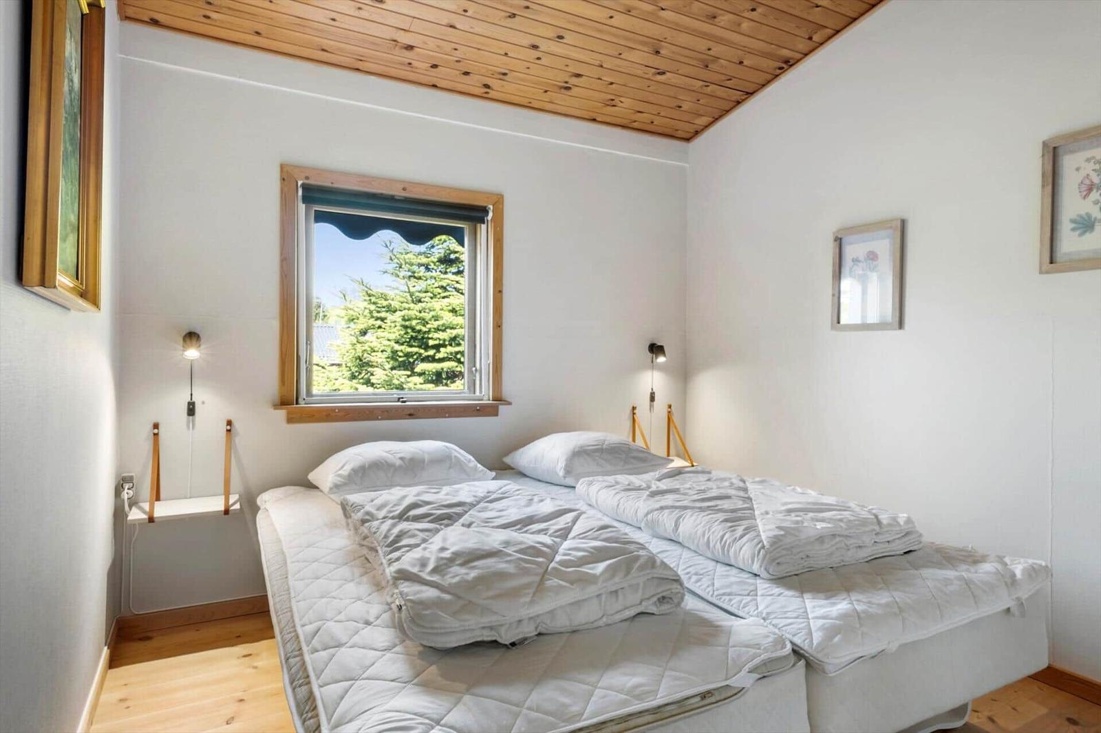 Bedroom with double bed, wooden ceiling, and window with view of trees.