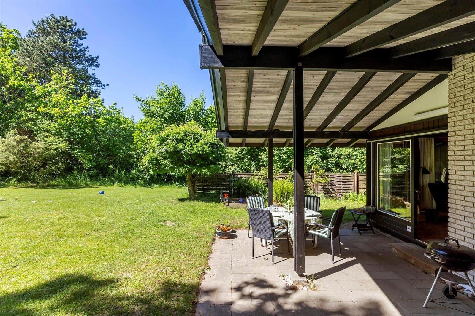 Patio with table and chairs, grill, and view of green lawn.