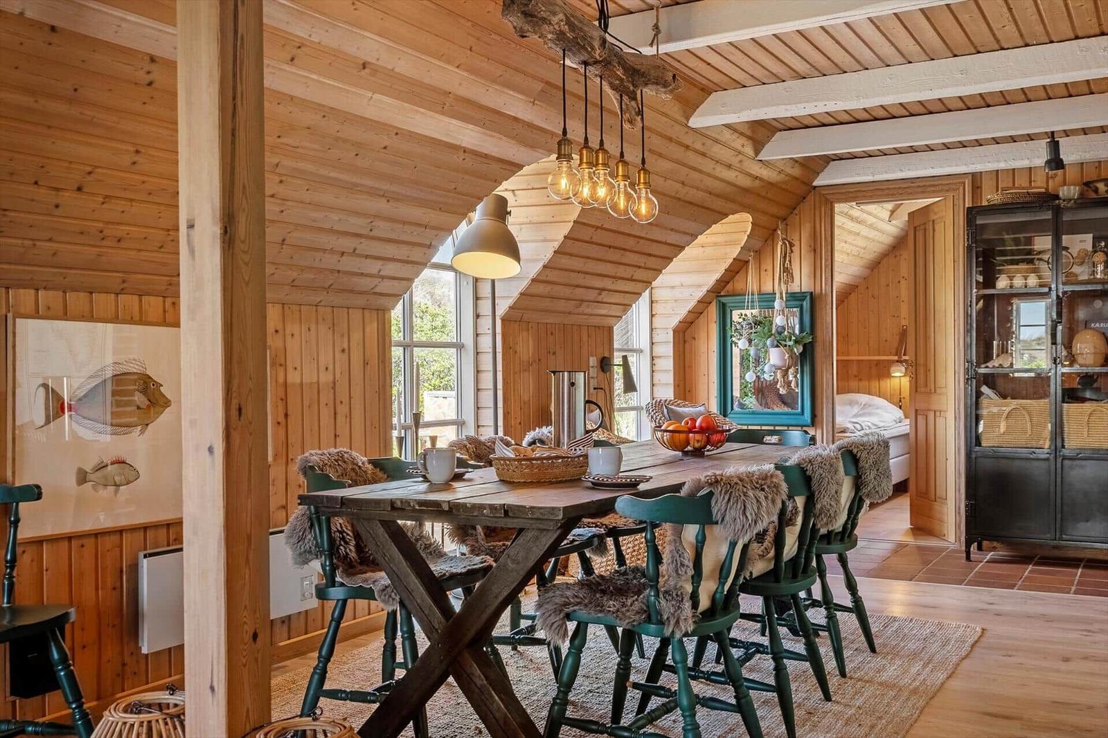 Dining area with wooden table, green chairs with fur trim under wooden ceiling.