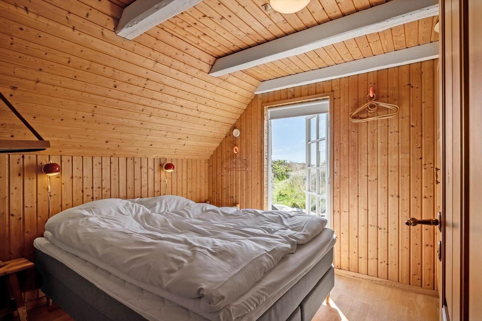 Bedroom with wooden walls, bed, and window with view outside.