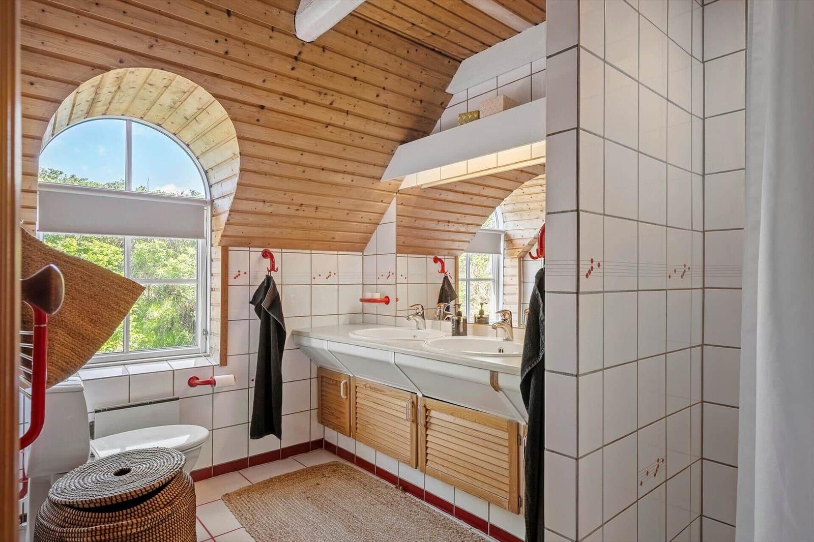Bathroom with double sink, wooden ceiling, and bathroom window with view of greenery.