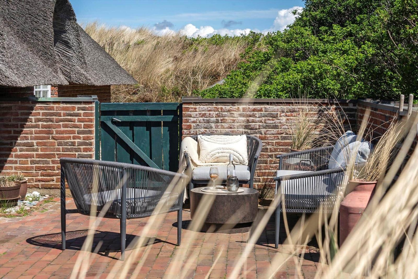 Terrace with seating group, table, and view of grass and planting.