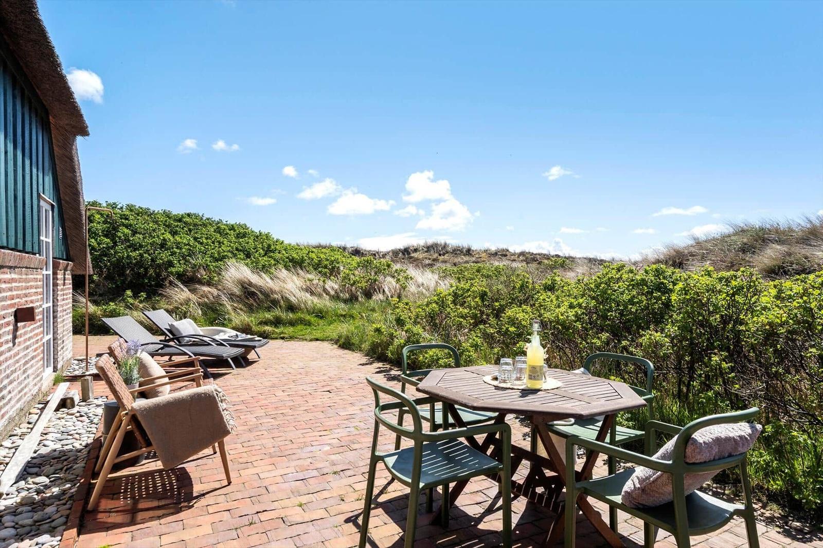 Terrace with table, chairs, and loungers. View of greenery and sky.