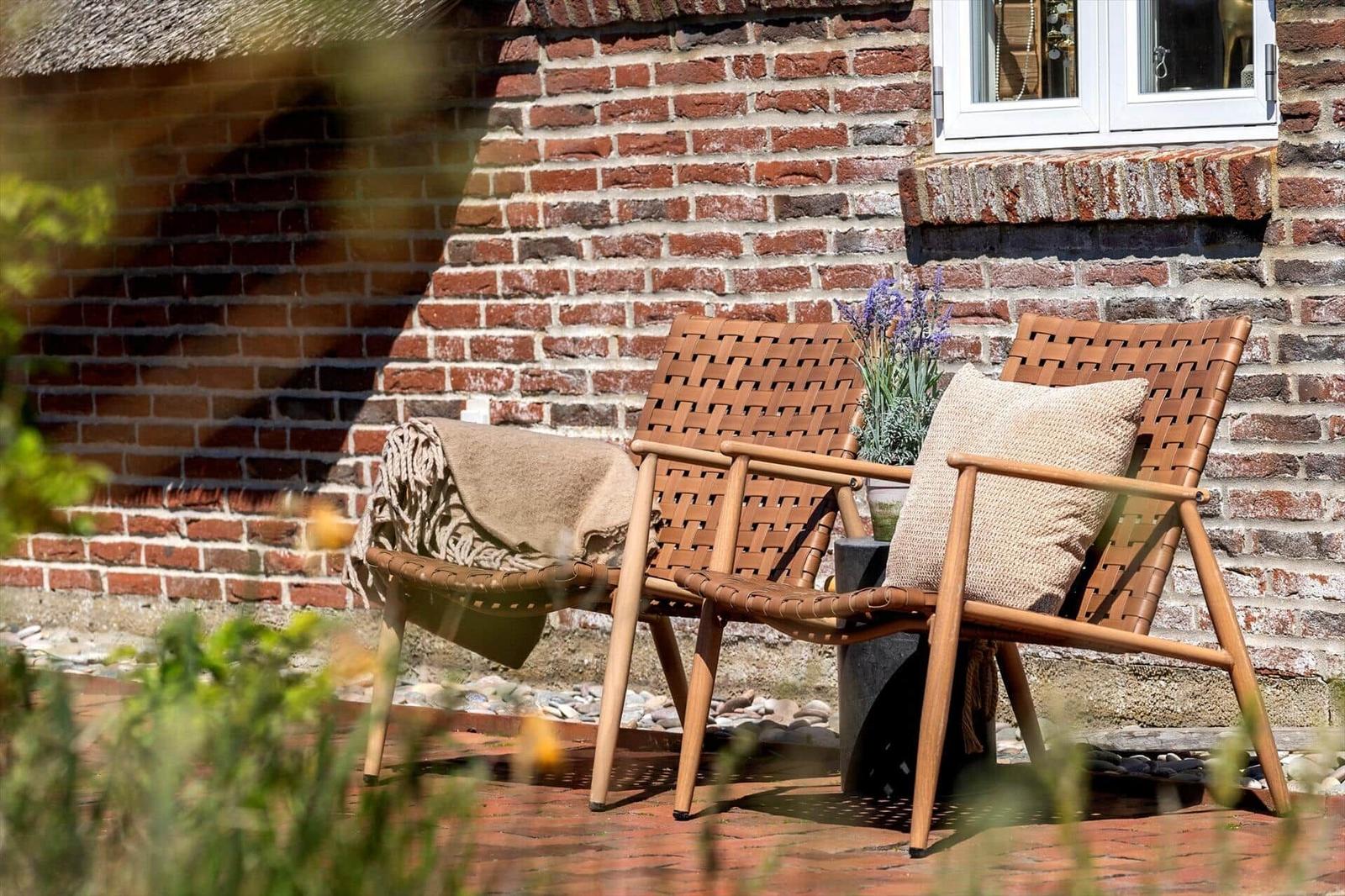 Two chairs with cushions and a blanket stand against a brick wall.