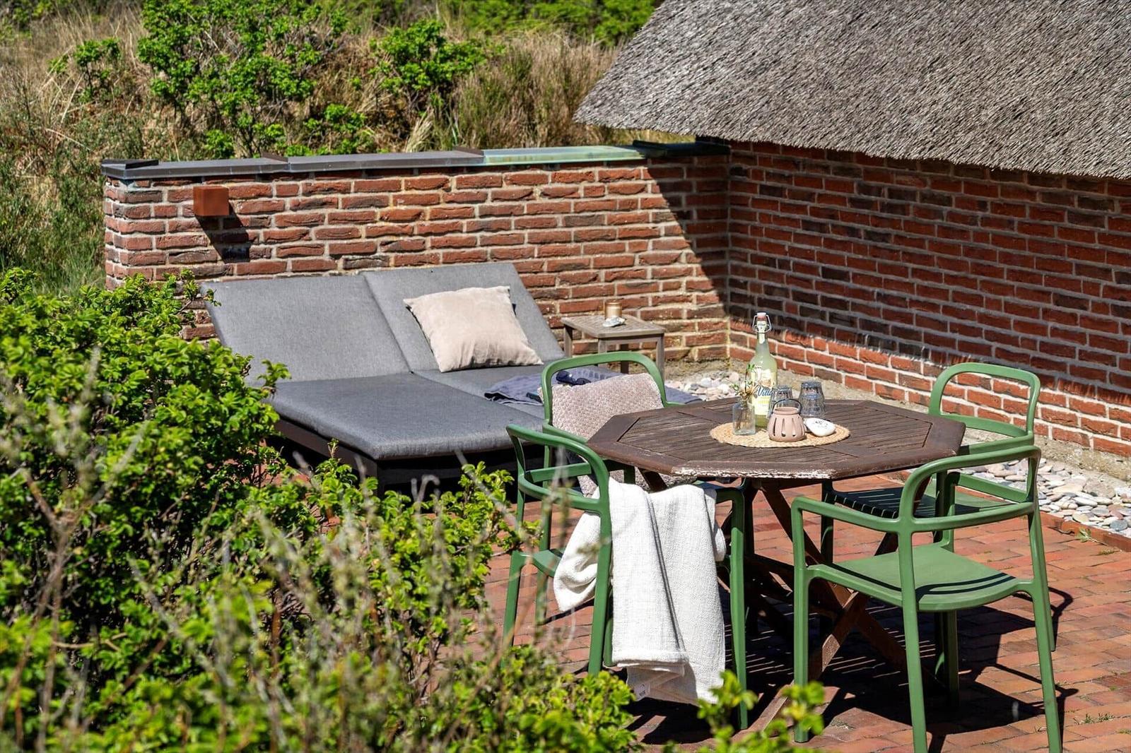 Terrace with seating group, table and chairs next to red brick wall.