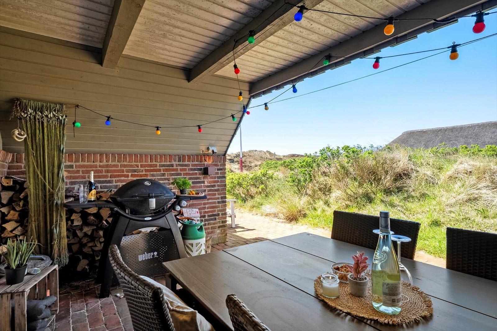 Terrace with grill, table and chairs under colorful string lights. View of green dunes.