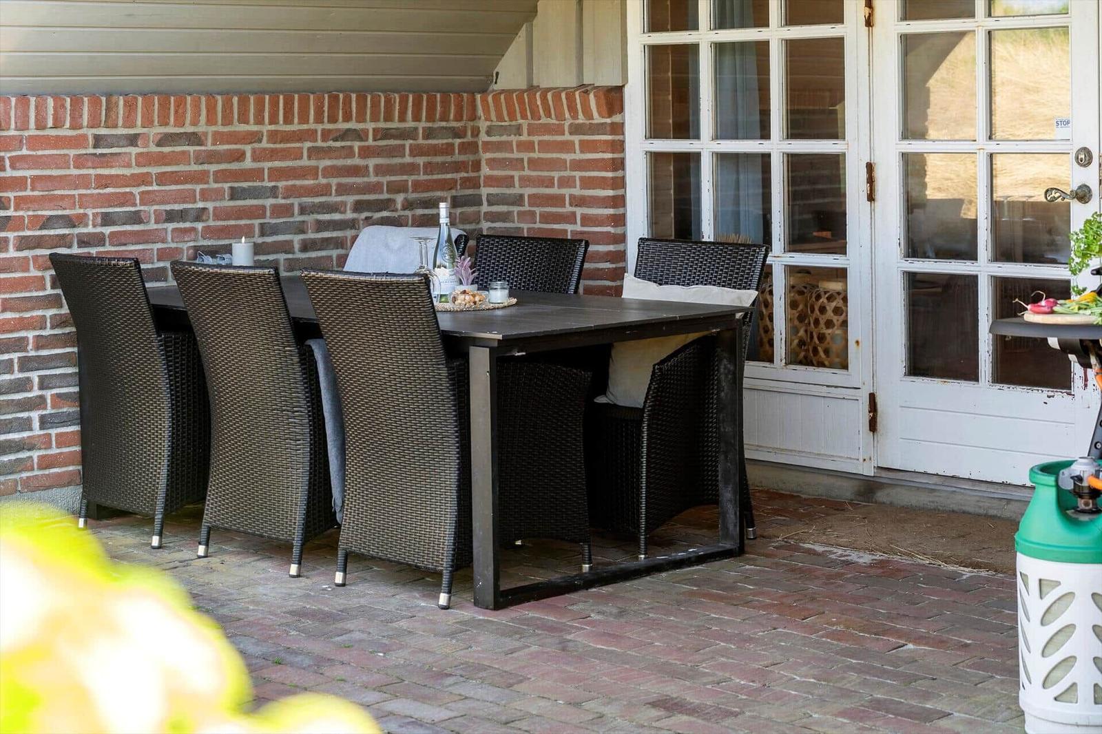 Patio with dining table and chairs in front of brick wall and white doors.