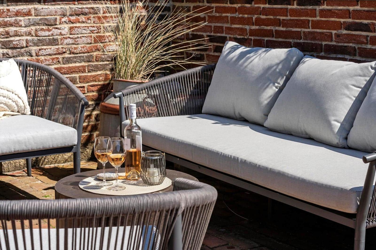 Outdoor area with sofa, chairs, and table. On the table are glasses and a bottle.