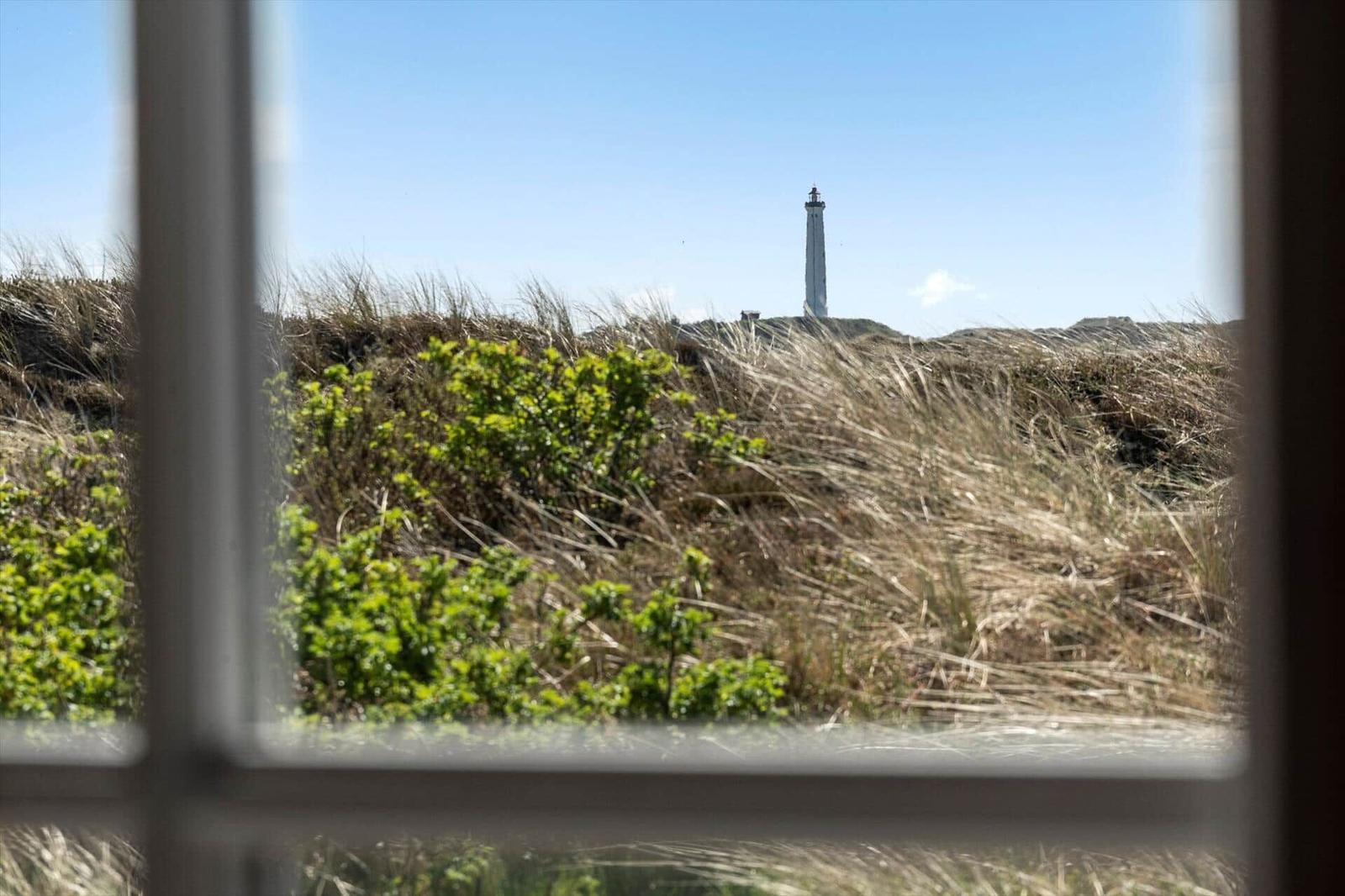 View through a window of a lighthouse behind dunes and grasses.