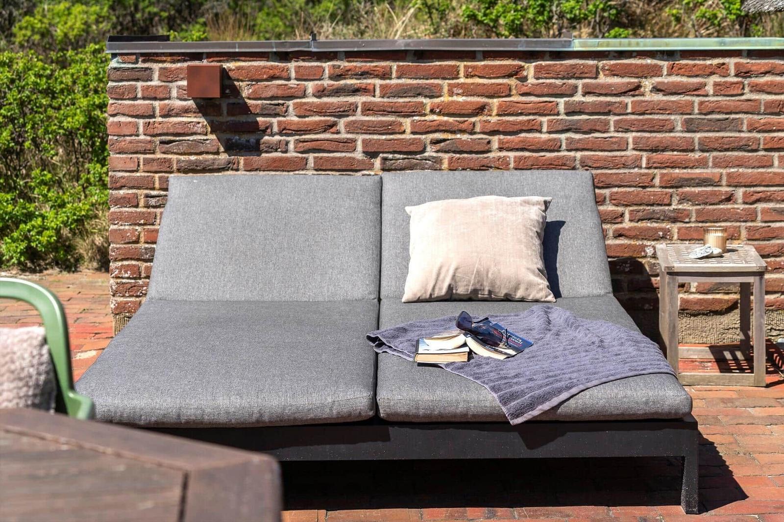 Outdoor terrace with gray lounge sofa, pillow, blanket, and table.