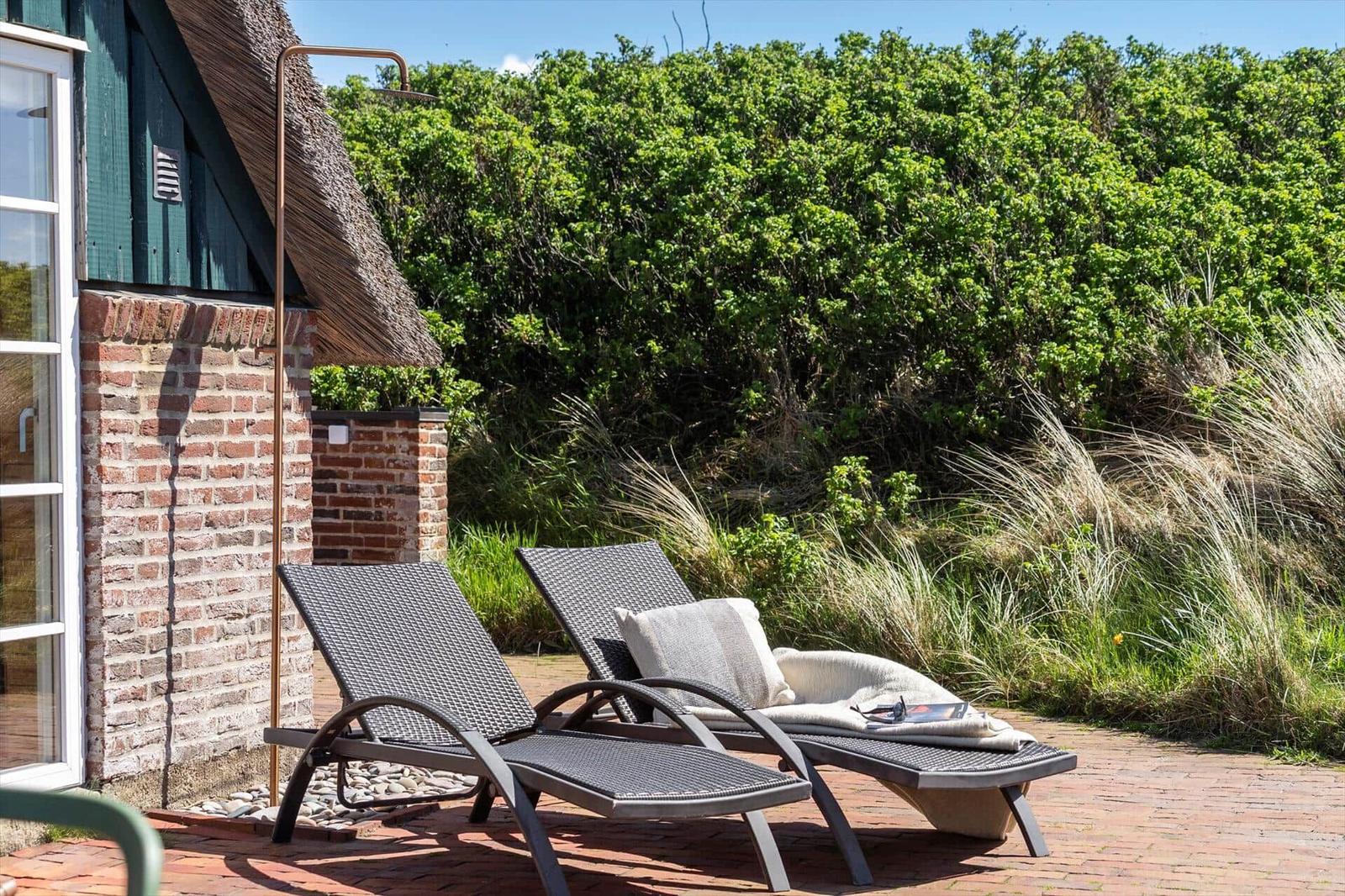 Two lounge chairs on terrace beside house with thatch roof and greenery.