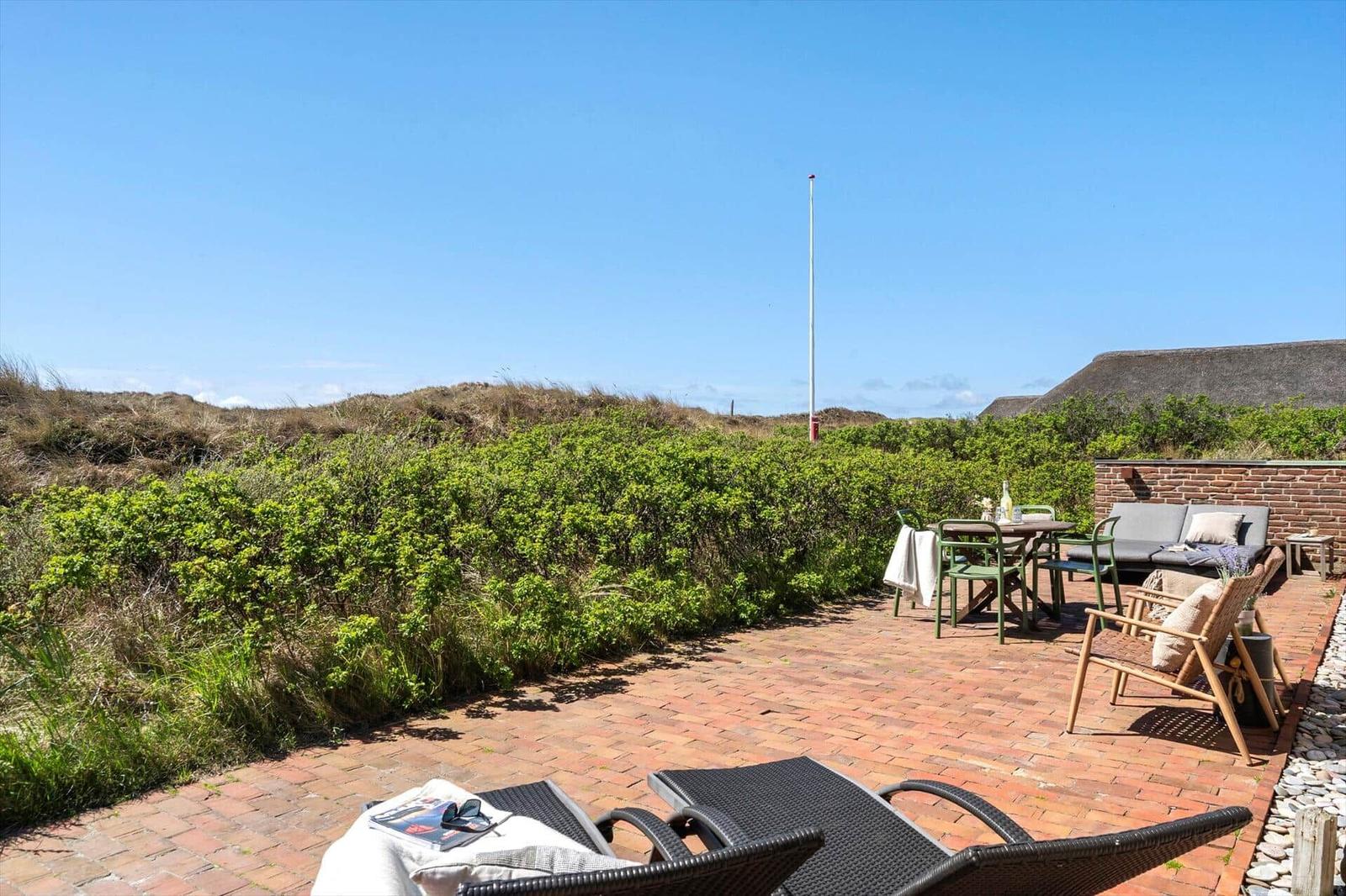 Terrace with loungers, table, and seating. Greenery and sand dunes in the background.