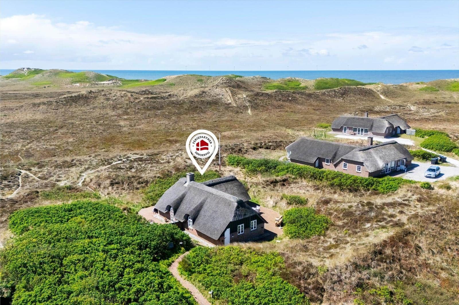 Three houses with thatched roofs are situated on dunes with a view of the sea.