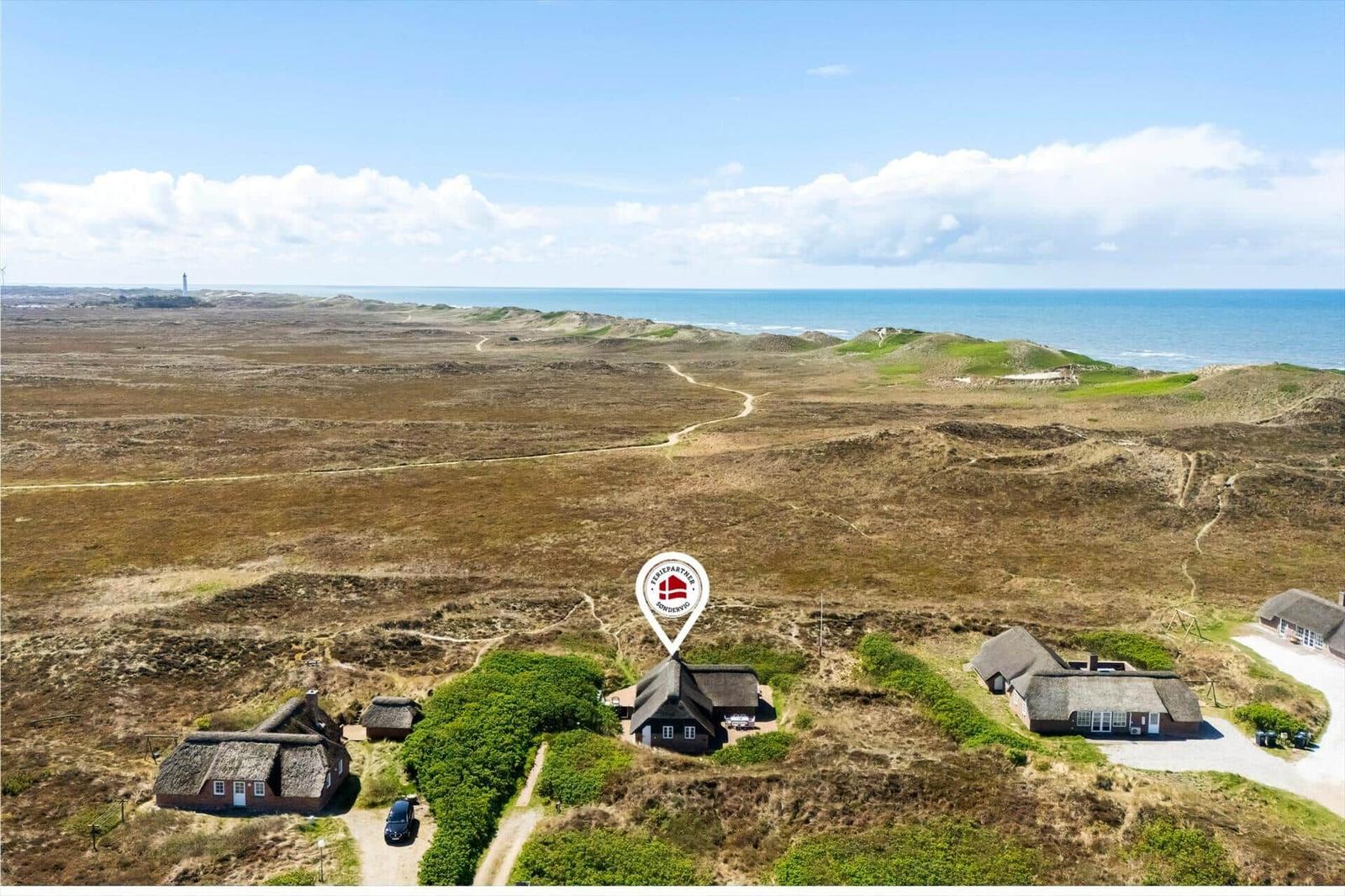 House with thatched roof in dune landscape, view of sea and lighthouse