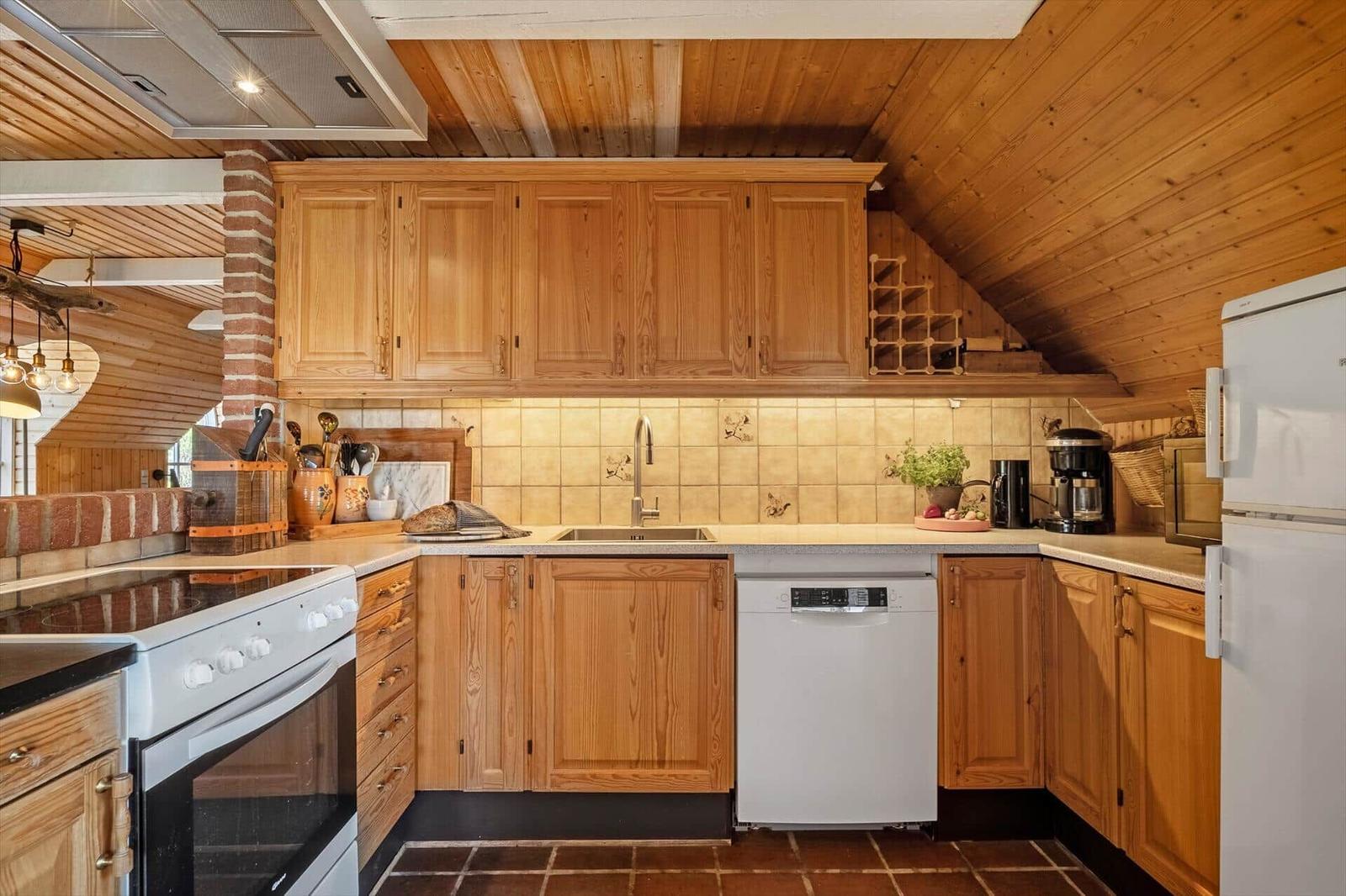 Kitchen with wooden cabinets, tile backsplash, and modern appliances under a sloped wooden ceiling.