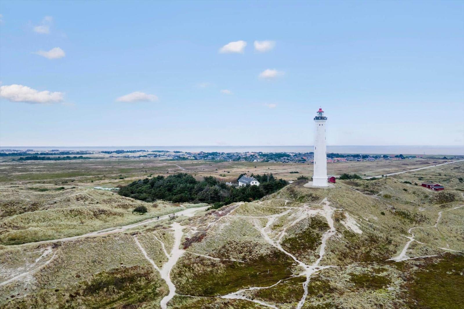 White lighthouse on dunes with view of coastal landscape and sky.