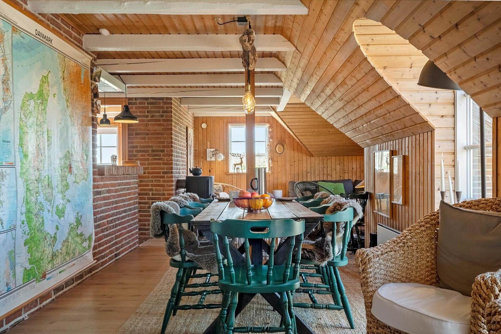 Dining room with wooden ceiling, large table, and green chairs. Wall map of Denmark.