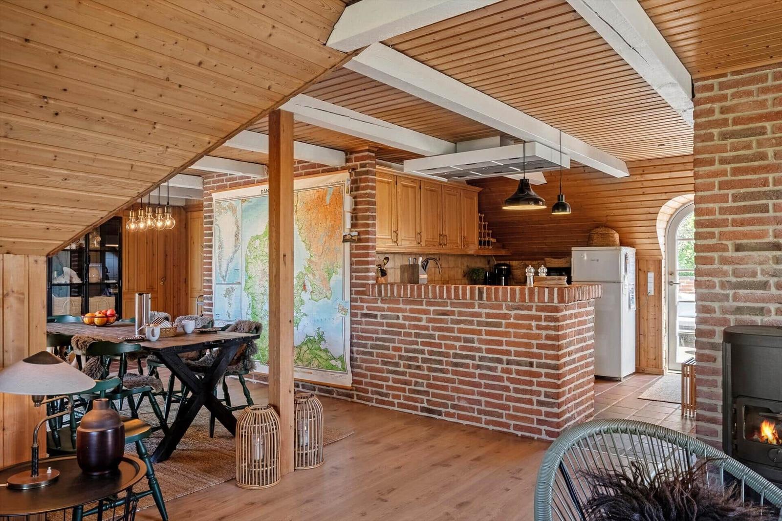 Kitchen with brick wall, dining area, and wood-burning stove under wooden ceiling.