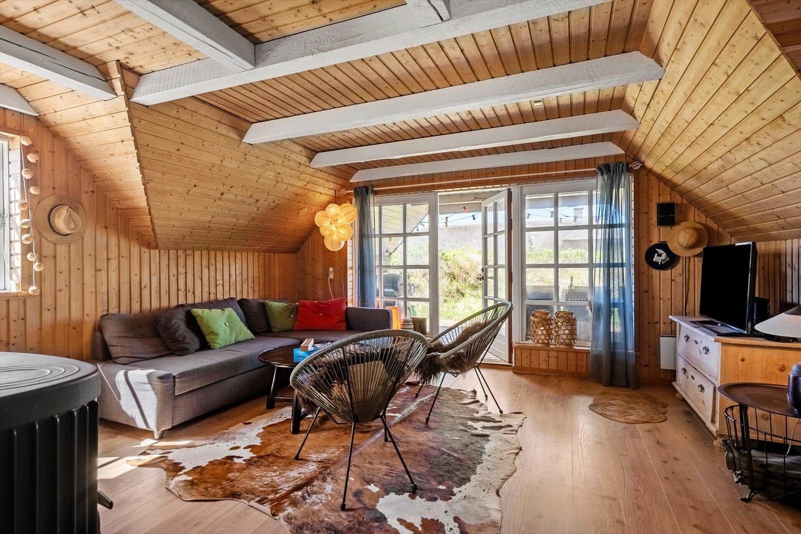 Living room with wooden ceiling, sofa, chairs, and windows to terrace.