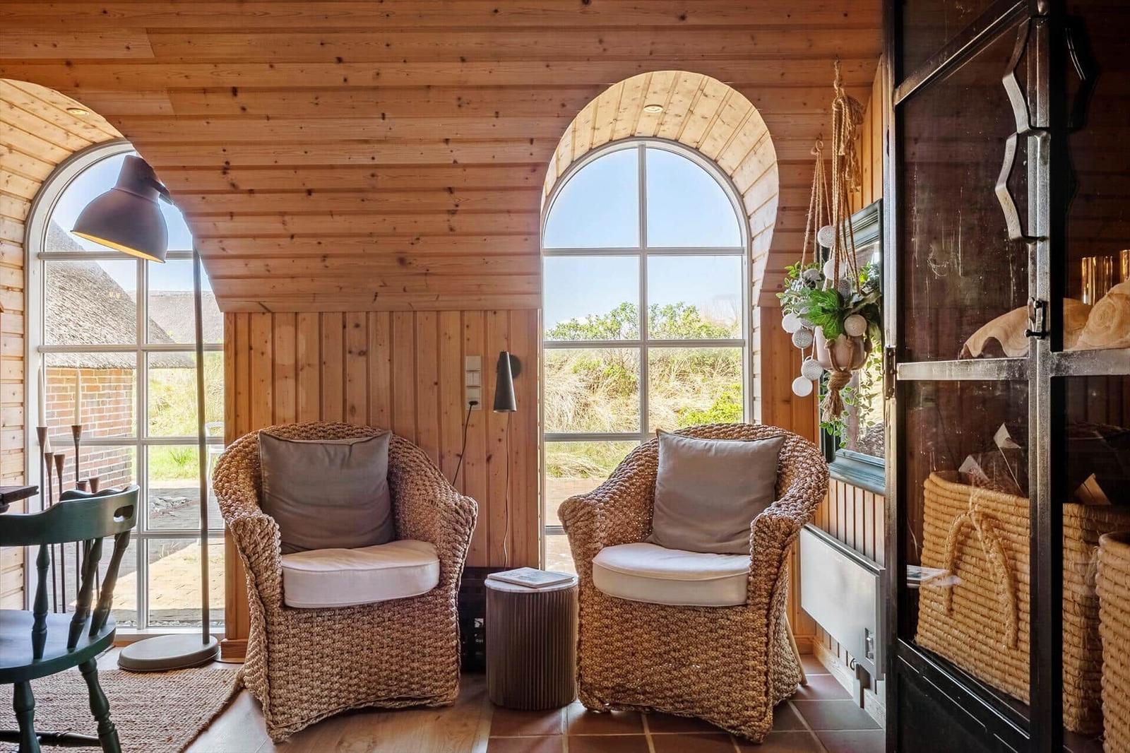 Two woven chairs stand under arched windows with wood paneling.