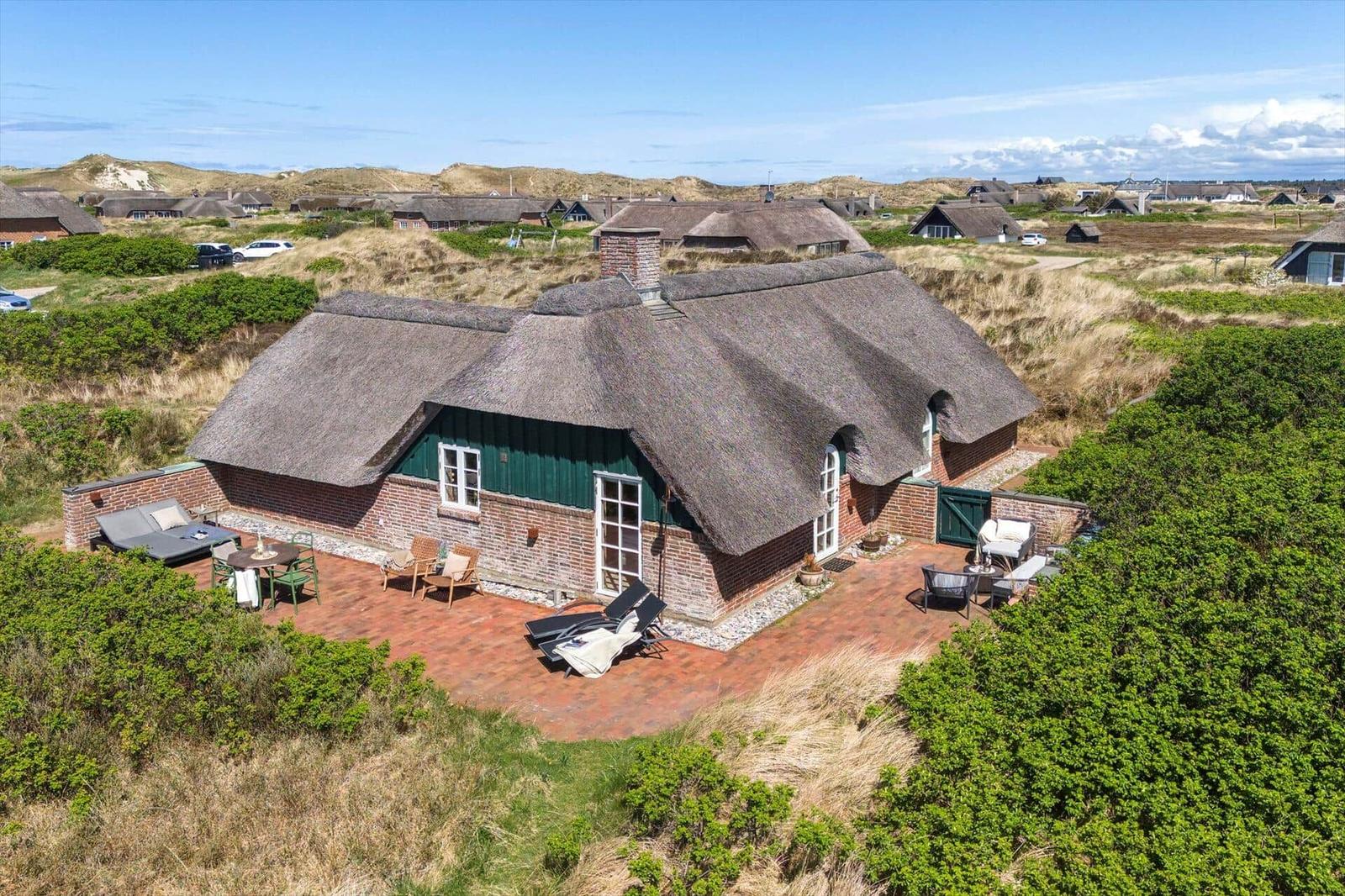 Thatched-roof cottage with terrace and garden. View of dune landscape.