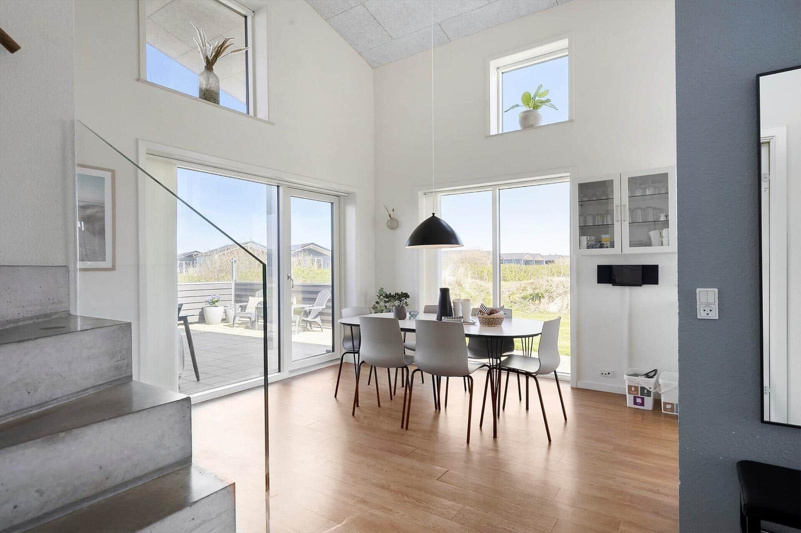 Essbereich mit Tisch, Stühlen und Glasfront zur Terrasse. Helle Wände und Holzboden.