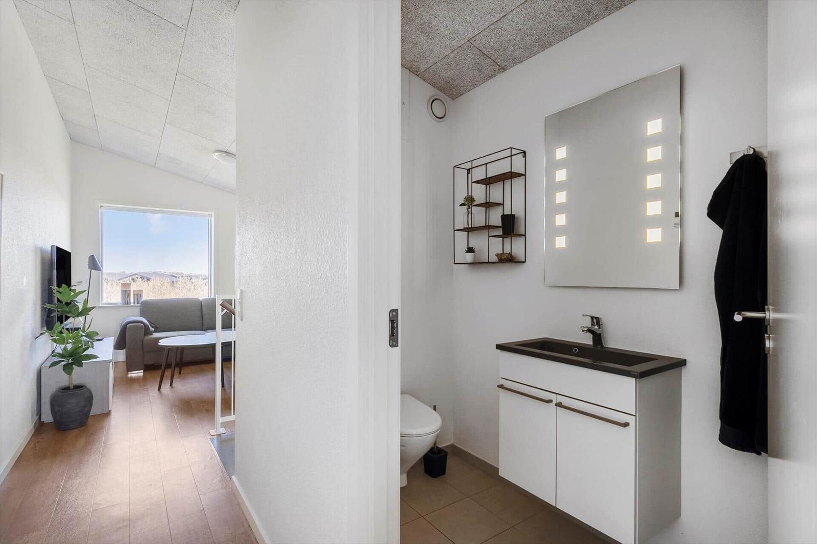 Badezimmer mit Spiegelschrank und Waschtisch. Wohnzimmer mit Sofa und Fenster.