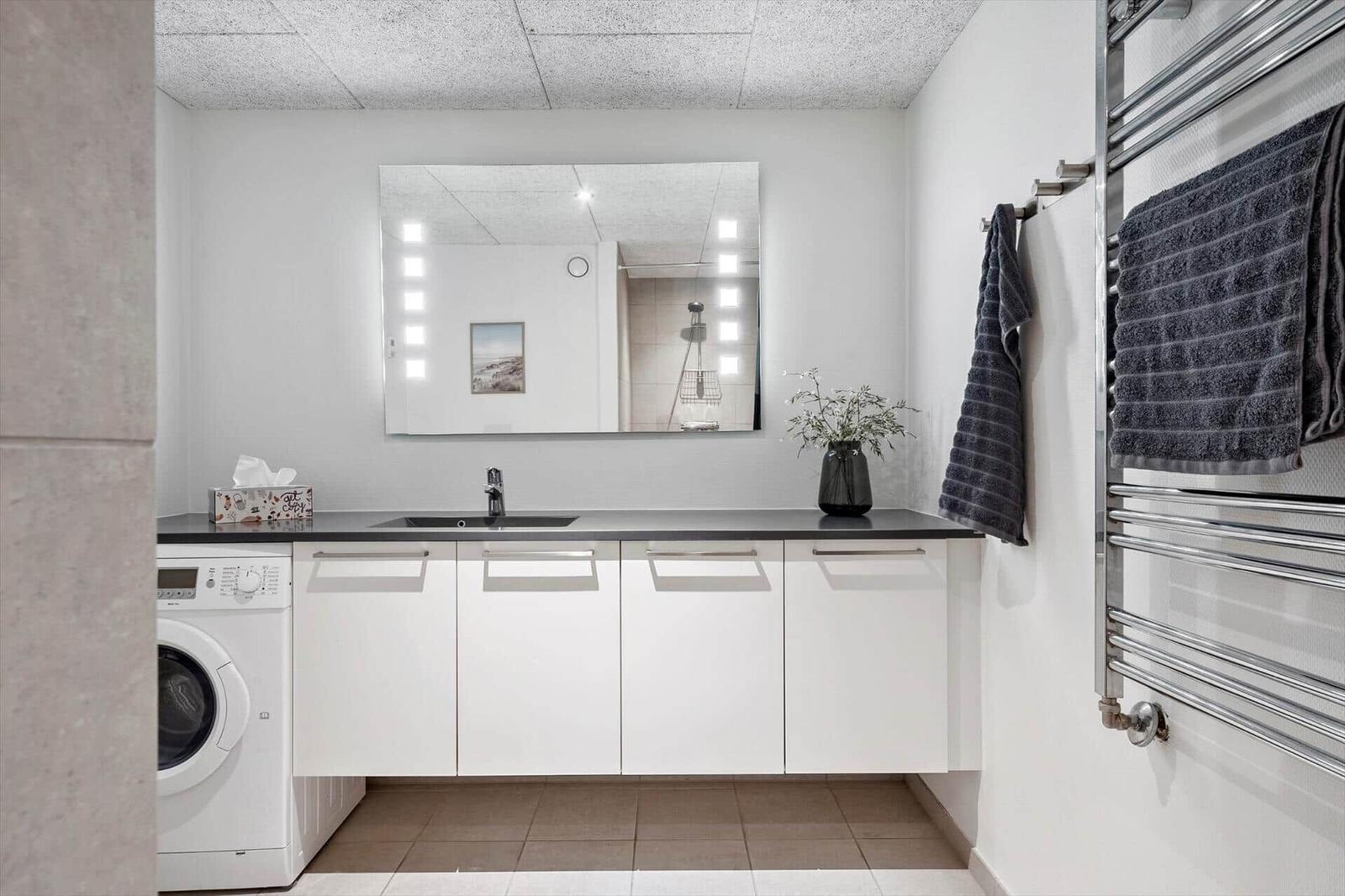 Badezimmer mit Waschmaschine, Spiegel und Handtuchheizung.