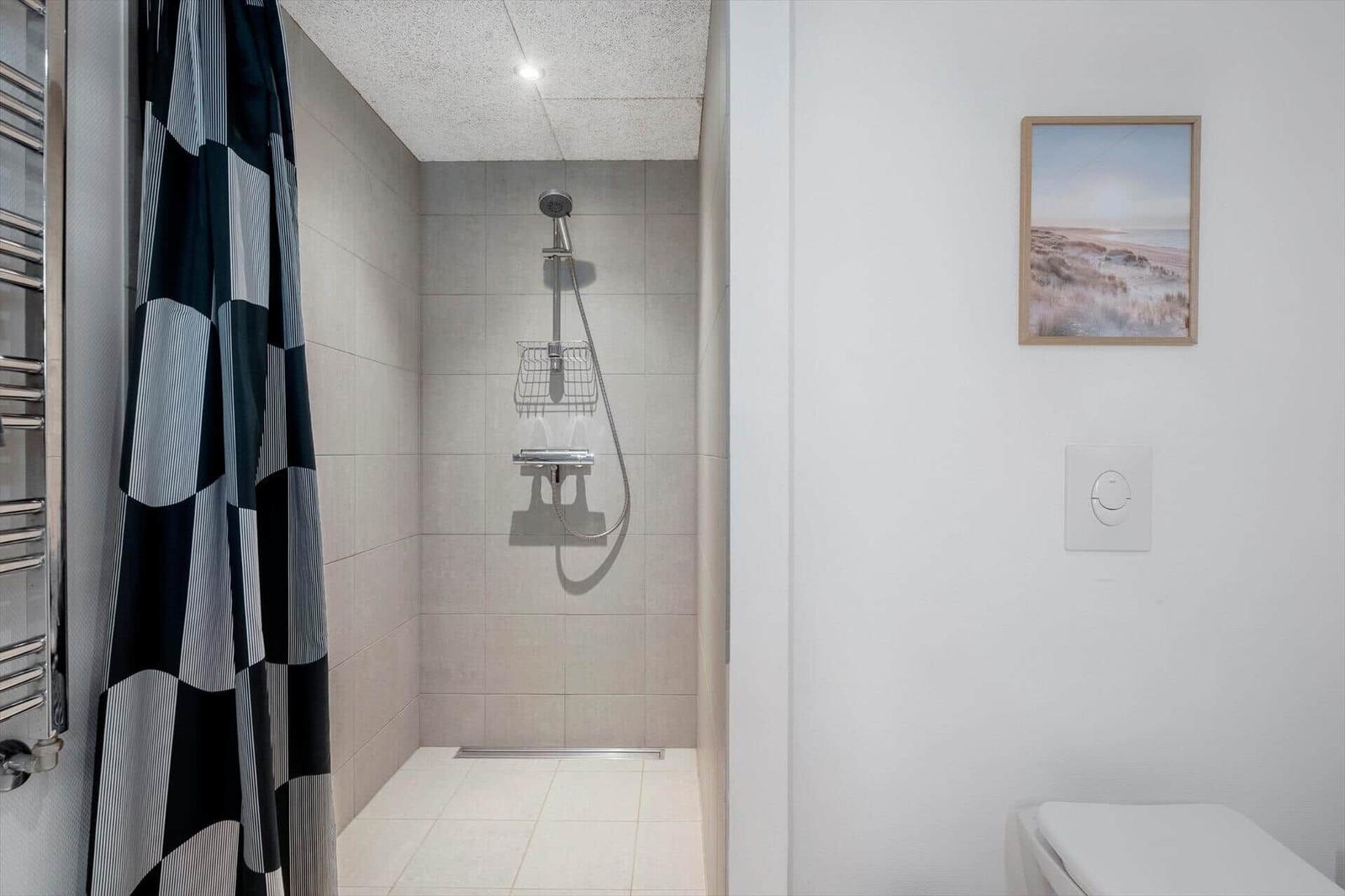 Dusche mit Duschvorhang, Wandbild und Toilette.