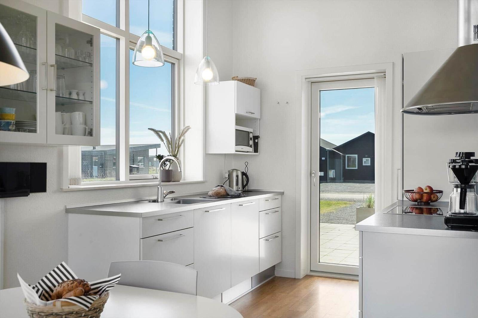Küche mit weißen Schränken, Fenster und Tür zur Außenterrasse.