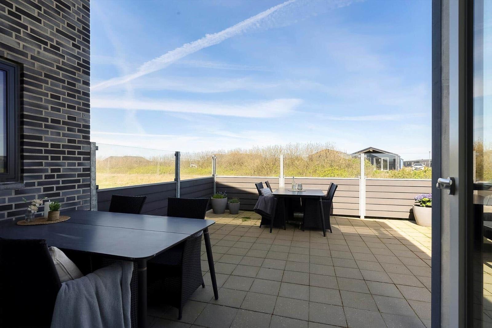 Terrasse mit Tisch und Stühlen, Blick auf Felder und Himmel.