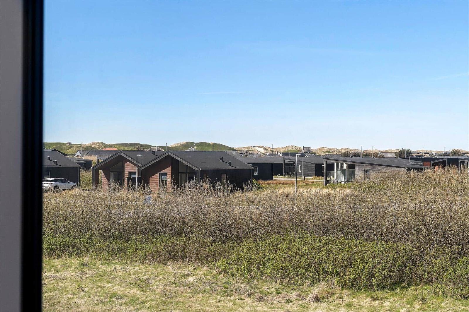 Ansicht von Ferienhäusern mit Dach und Fenstern hinter Buschwerk und Gras.