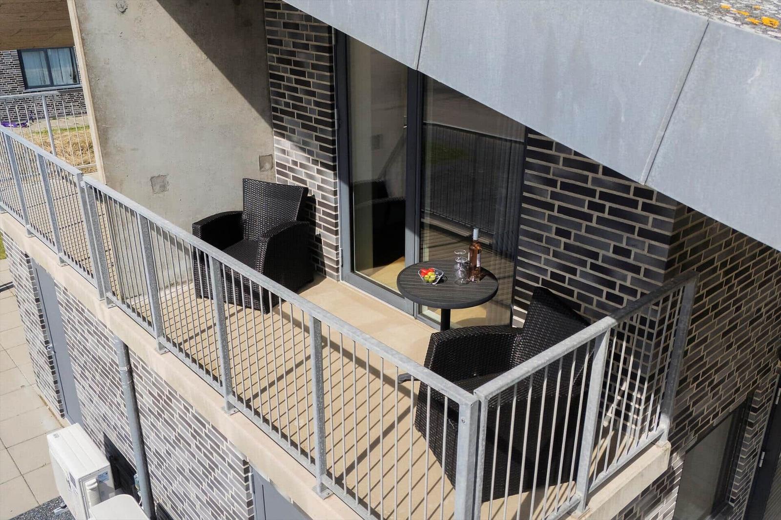 Terrasse mit Tisch und zwei Stühlen, Glasfront und Ziegelwand