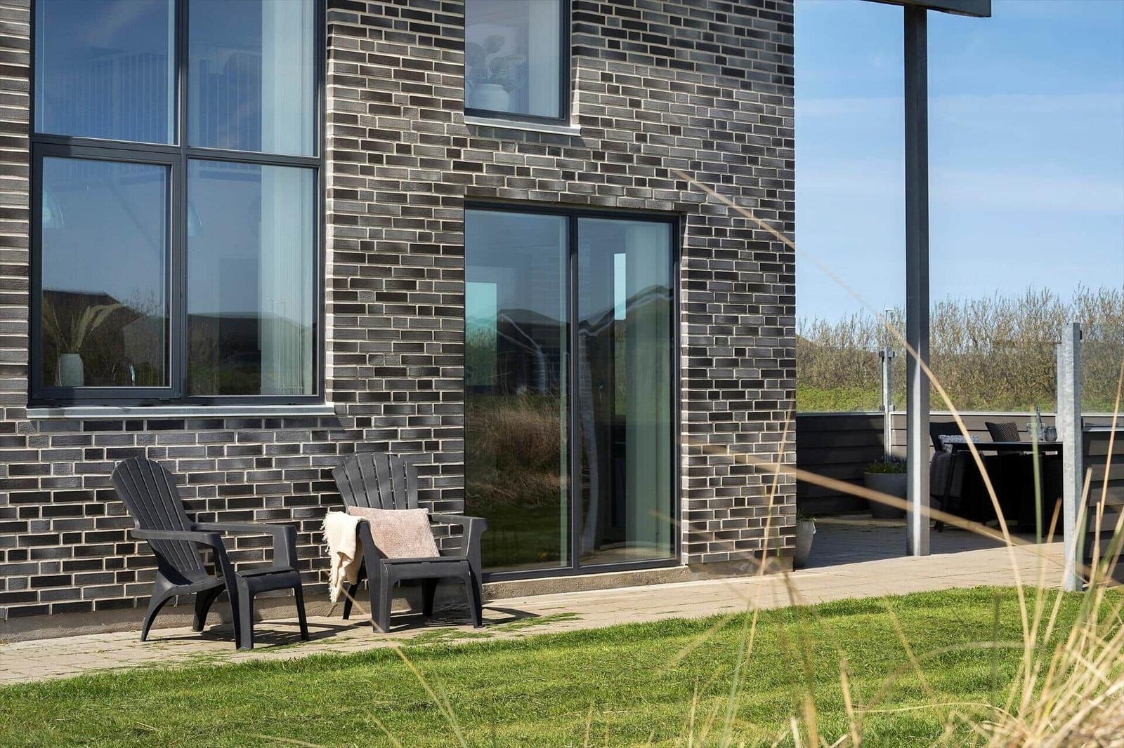 Terrasse mit zwei Stühlen vor einem Haus mit dunklem Ziegel und großen Fenstern.