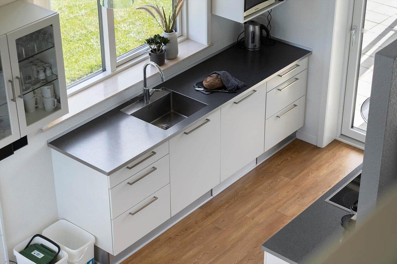 Küche mit weißen Schränken, dunklem Arbeitsplatz und Fensterblick auf Gras.